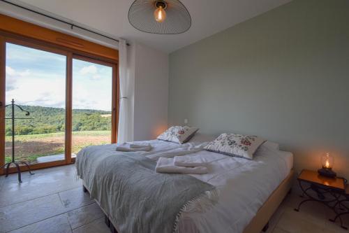 a white bedroom with a bed with a large window at Domaine d'Essendiéras in Saint-Médard-dʼExcideuil