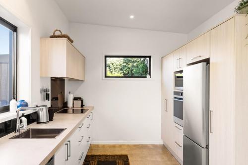 a kitchen with white cabinets and a stainless steel refrigerator at 120m to Wainui Beach - Modern Coastal Unit in Gisborne