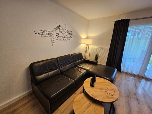Ferienhaus Nr 96, Kategorie Komfort Plus, Feriendorf Hochbergle, Allgäu في Karlsebene: غرفة معيشة مع أريكة جلدية سوداء وطاولة