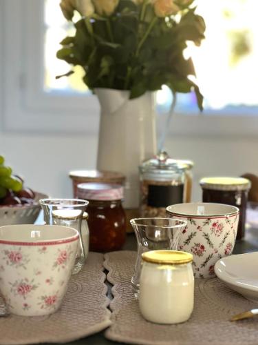 una mesa cubierta con tazas y un jarrón con flores en La Chambre d'hôte de Manou en Normandie, en La Noë-Poulain