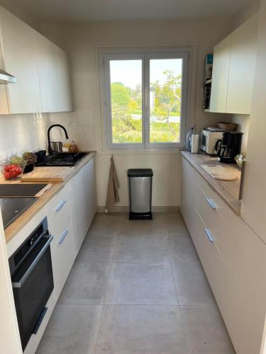 une cuisine avec des armoires blanches, un évier et une fenêtre dans l'établissement La Bretonne vue mer, à Lanmodez