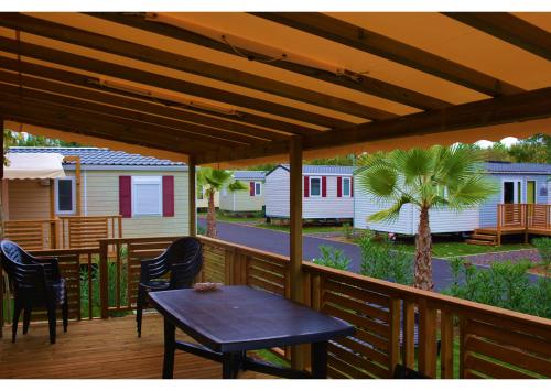 une terrasse en bois avec une table, des chaises et des maisons dans l'établissement Mobil home - Clim, LV, LL, TV - Camping LA CARABASSE 4 étoiles - MH-A004, à Vias