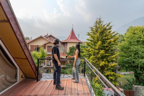 a man and woman standing on the balcony of a house at SaffronStays The Divine Hima in Dharamshala