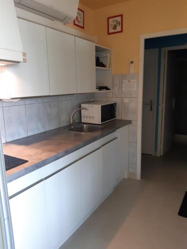 une cuisine avec des armoires blanches, un évier et un micro-ondes dans l'établissement Quartier Point Zéro appartement studio pour 5 personnes N3, à La Grande Motte