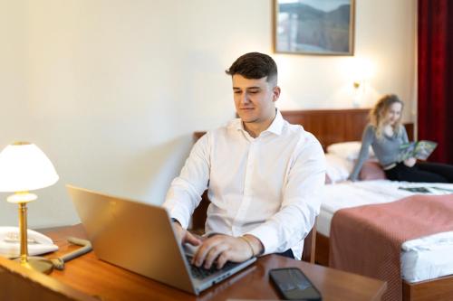a man sitting at a desk with a laptop in a hotel room at Hotel Pannonia in Miskolc