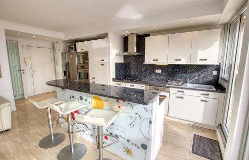 une cuisine avec des armoires blanches et un comptoir avec des tabourets dans l'établissement Le Clair Golfe-Juan - T2 terrasse vue mer Parking privé WIFI - LIMESTAY, à Vallauris