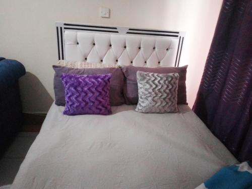 a bed with purple and purple pillows on it at Kahawa Wendani Maguna's Supermarket Apartments in Nairobi