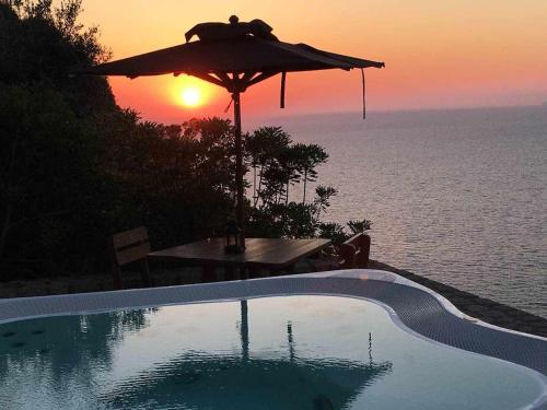 a pool with an umbrella and a table with the sunset at Villa DAlessandro in Anacapri