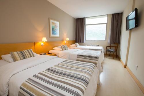 リオデジャネイロにあるAugusto's Rio Copa Hotelのベッド3台、薄型テレビが備わるホテルルームです。