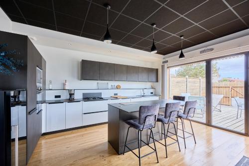 une cuisine avec des placards blancs et un comptoir avec des tabourets de bar dans l'établissement La Bouteille à la Mer-Maison darchitecte jacuzzi, à Barneville-Carteret