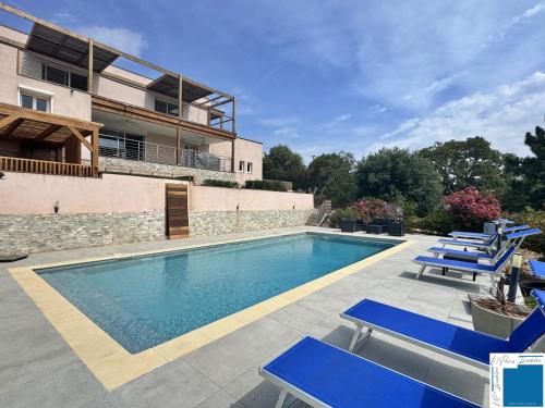 une piscine avec des chaises bleues et un bâtiment dans l'établissement VILLA GIULIA - Piscine - Jacuzzi - 4 Chambres, à Porto-Vecchio