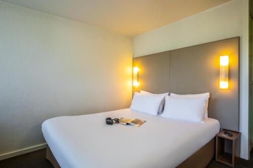 a white bed with two pillows and a book on it at Campanile Vichy - Bellerive in Bellerive-sur-Allier