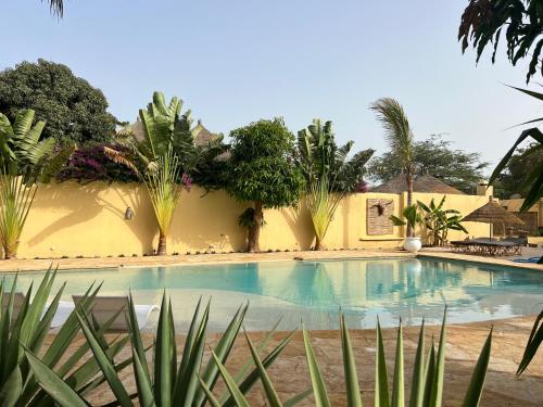 a swimming pool in front of a yellow building with plants at Adjana in Ngaring