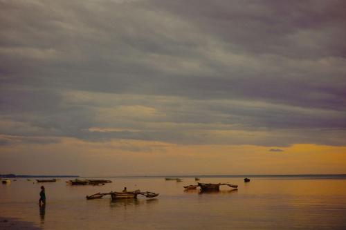 a man standing in the water with boats in the water at Cinnamon Hotel in Jambiani
