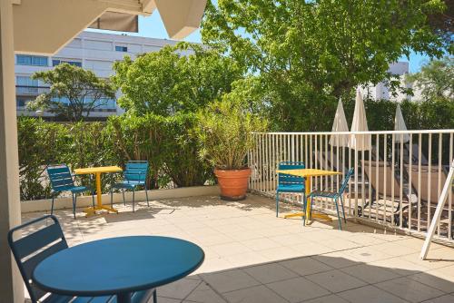 a patio with tables and chairs and a fence at Hôtel Les Rives Bleues in La Grande-Motte