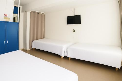a room with two beds and a tv on the wall at Hôtel Les Rives Bleues in La Grande-Motte