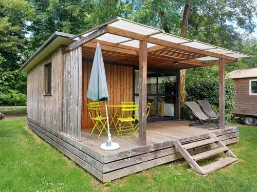 uma pequena cabana de madeira com cadeiras e um guarda-chuva em Huttopia Beaulieu sur Dordogne em Beaulieu-sur-Dordogne
