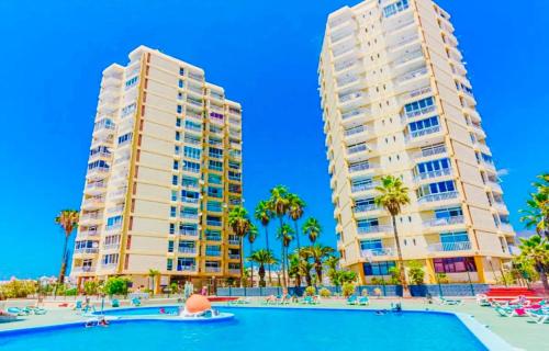 twee hoge gebouwen naast een zwembad met palmbomen bij Exclusive ocean front apartment in Playa de las Americas