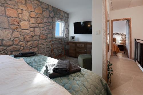 Dormitorio con pared de piedra, cama y TV en Villa Ana, en Prizna
