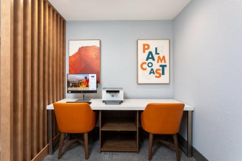a desk with a computer and two orange chairs at Holiday Inn Express & Suites Palm Coast - I-95 in Palm Coast