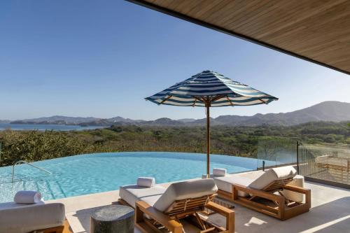 a pool with chairs and an umbrella next to a swimming pool at W Costa Rica Resort – Playa Conchal in Playa Conchal