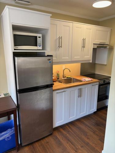 a kitchen with white cabinets and a stainless steel refrigerator at Pioneer Inn by the River in Port Hardy
