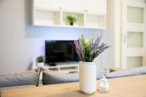 a white vase with purple flowers on a table at Baltic Cliff Apartment- Babie Doły in Gdynia
