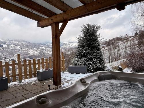 une baignoire assise sous une pergola en bois dans la neige dans l'établissement Aux Sources - 14 personnes - sauna & jacuzzi, à La Bresse