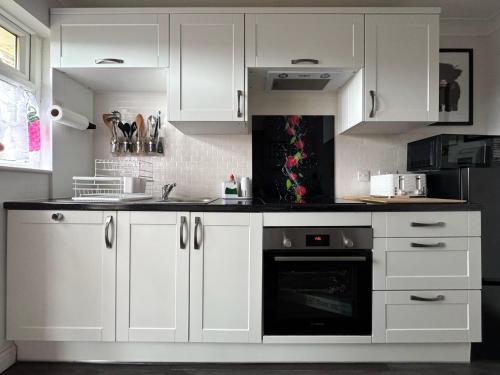 a kitchen with white cabinets and a black oven at FINN VILLAGE "Raspberry Cottage" Private Garden, 6-seater HOT TUB, Firepit & Pizza Stove in Drymen