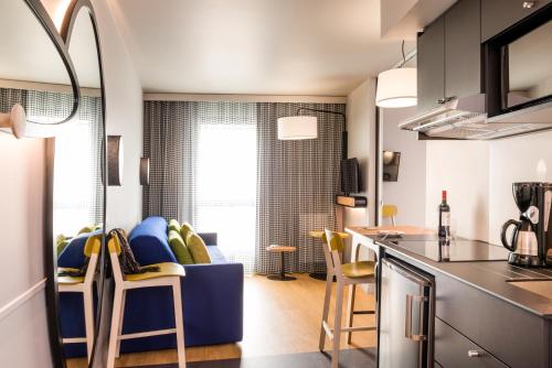 a kitchen and living room with a blue couch and chairs at Aparthotel Adagio access Colombes La Défense in Colombes