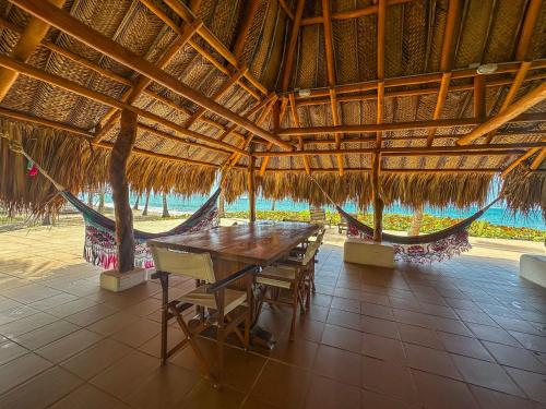 a table and chairs in a straw hut with a hammock at Hotel Chiniu in Palomino