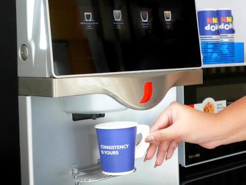 a person is holding a cup under a coffee maker at HOP INN Saraburi in Sara Buri