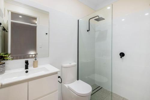 a white bathroom with a toilet and a shower at Tigerlily's in Byron Bay