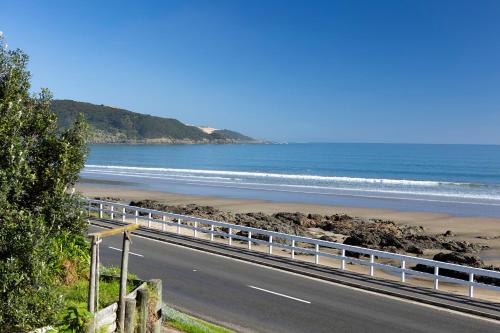 a road next to a beach with the ocean at Te Hu - Ahipara Beachfront Bach in Ahipara