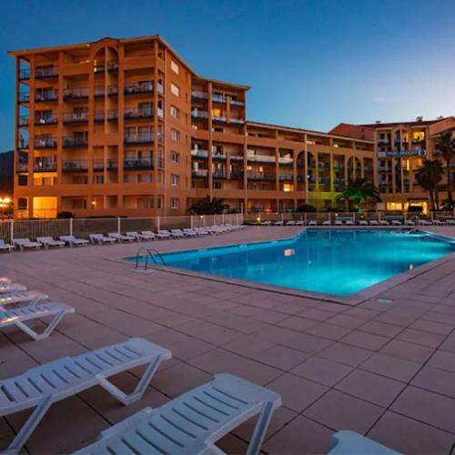 une piscine avec des chaises et un grand bâtiment dans l'établissement Résidence Mer & Golf Confort 3étoiles avec Piscine et Terrasse, à Argelès-sur-Mer