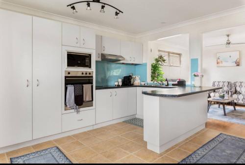a kitchen with white cabinets and a black counter top at The Urban Cozy Cottage - 5 Mins to Parramatta or Westmead Hospital or WSU in Wentworthville