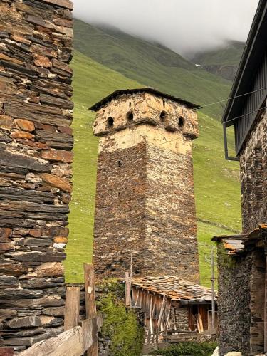 an old brick building with a green hill in the background at Nizharadze's Tower in Ushguli