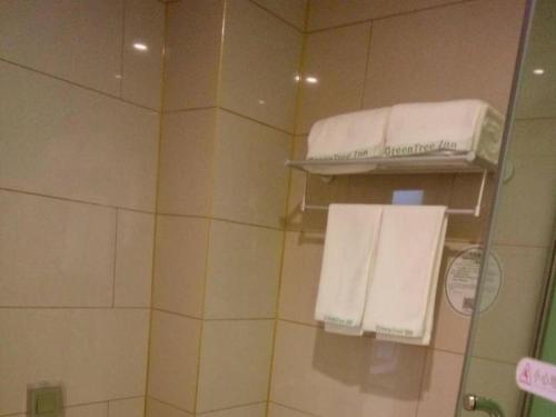 a bathroom with two white towels on a shelf at GreenTree Inn Qingdao Jiaozhou Jiaoping Road Express Hotel in Qingdao