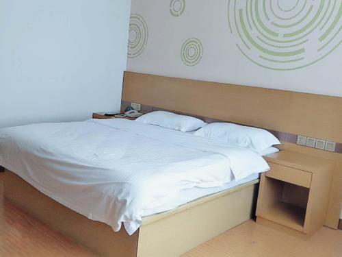 a bedroom with a white bed with a night stand at GreenTree Inn Qingdao Jiaozhou Jiaoping Road Express Hotel in Qingdao