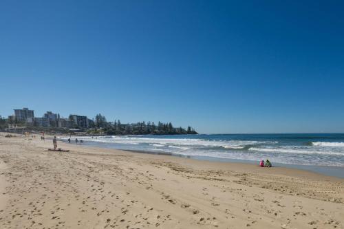 a beach with people sitting on the sand and the ocean at Tides and Tranquility at Kings Beach in Caloundra