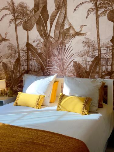 un lit avec des oreillers jaunes et un mur avec des palmiers dans l'établissement Les Cactus Fréjus Plage, à Fréjus