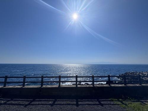 a sun shining over the ocean with a fence at Villa Thalassa 貸切 in Oshima