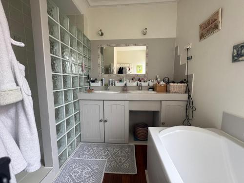 une salle de bain avec une baignoire, un lavabo et un miroir dans l'établissement Notre maison de famille, à Montmerle Sur Saône
