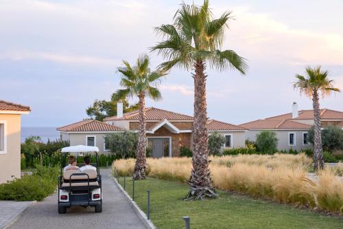 two people riding a golf cart in front of a house at Ajul Luxury Hotel & Spa Resort, a Registry Collection Hotel in Agia Paraskevi