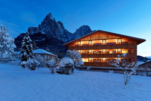 a large wooden building in the snow with a mountain at Artnatur Dolomites Hotel & Spa in Siusi