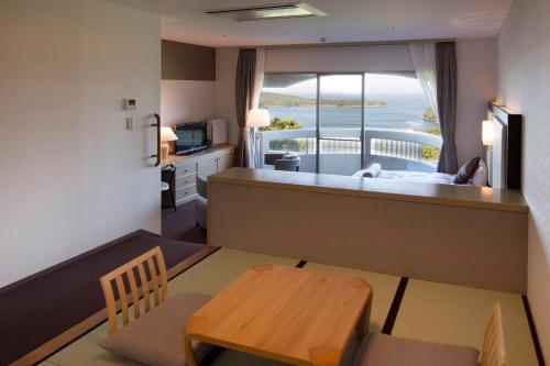 a room with a bed and a table and a balcony at Izumigo Hotel Altia Toba in Toba