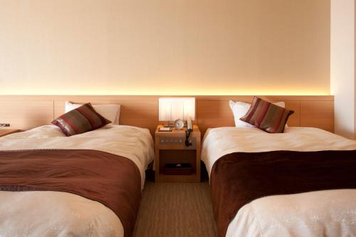 a hotel room with two beds and a table with a lamp at Izumigo Hotel Altia Toba in Toba