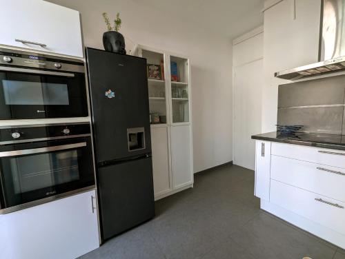 Il comprend une cuisine équipée d'un réfrigérateur noir et de placards blancs. dans l'établissement Appartement familial - Vue mer, à Bastia