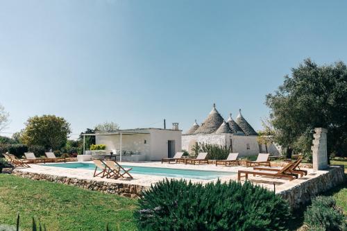 a swimming pool with benches and a house at Trullo dei Cinque in Cisternino