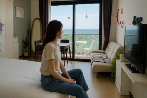 a woman sitting on a bed looking out at the ocean at Yeosu UTOP UBLESS All Rooms Stunning Ocean View in Yeosu